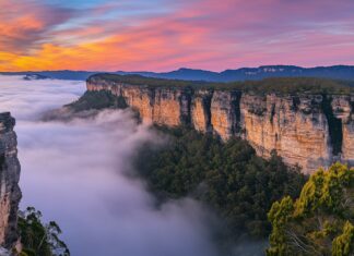 A dramatic mountain landscape desktop wallpaper with layers of fog rolling over rocky cliffs at sunrise.