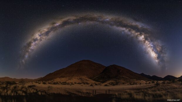 A dramatic mountain range under a starry night sky illuminated by the Milky Way.