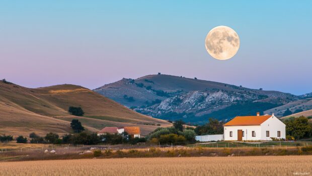 A full moon casting its soft light over a picturesque countryside, with rolling hills, a quaint farmhouse, and a calm, starry night.