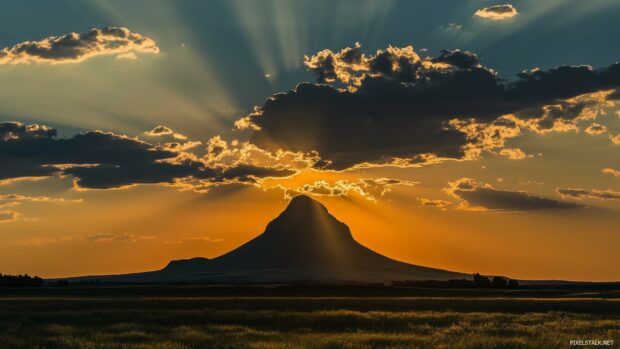 A lone Mountain silhouetted against a dramatic sunset, with rays of light streaming through scattered clouds.