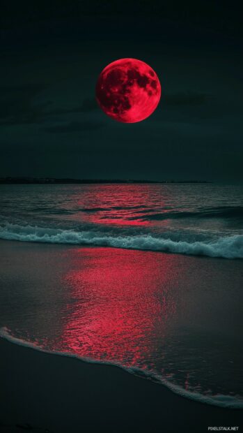 A mesmerizing red moon hanging low in the night sky over a tranquil beach.