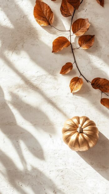 A minimalist Thanksgiving iPhone background featuring a delicate gold pumpkin and elegant autumn leaves.