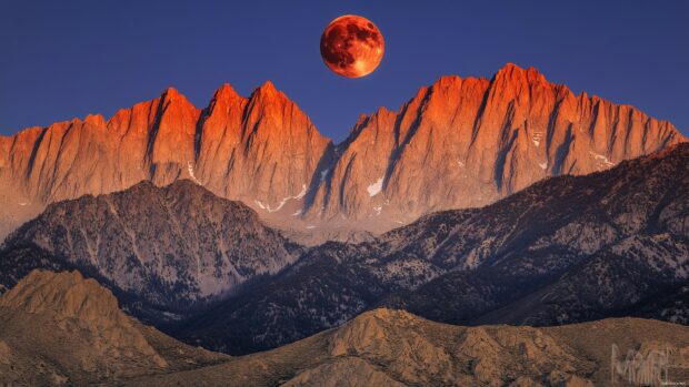 A red moon setting behind a rugged mountain range, 4K wallpaper for desktop.