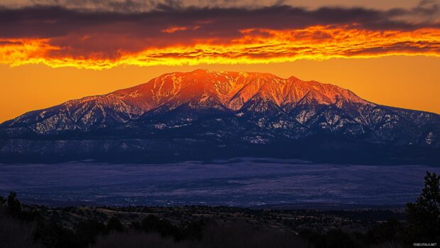 A rugged snowy peak surrounded by golden clouds during a fiery sunset.