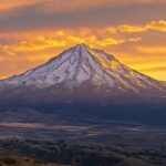 A rugged snowy peak surrounded by golden clouds during a fiery sunset.