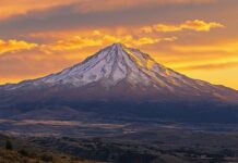 A rugged snowy peak surrounded by golden clouds during a fiery sunset.