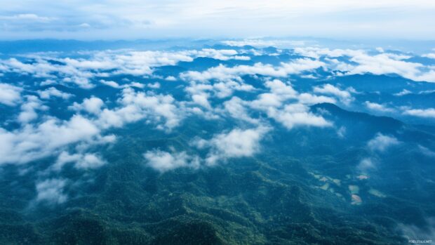 A serene mountain landscape wallpaper HD with low lying clouds drifting over emerald green valleys.