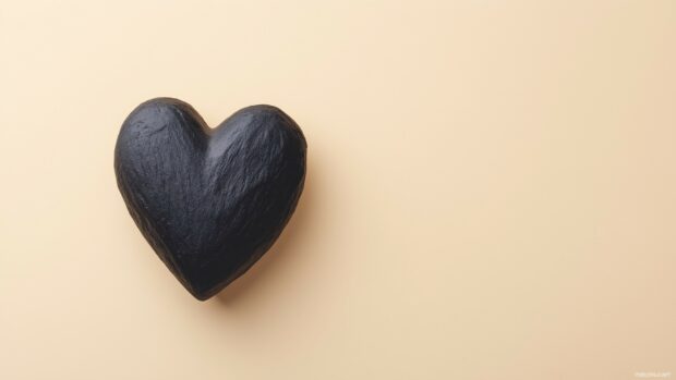 A single, textured black heart placed off center on a pale beige background.