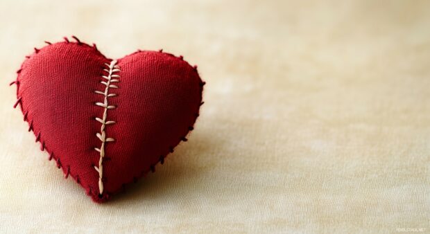 A stitched up heart HD wallpaper with visible thread along the crack, placed on a soft cream background.