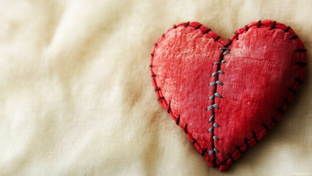 A stitched up heart with visible thread along the crack, placed on a soft cream background.