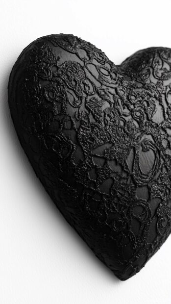 A textured black heart with intricate lace patterns set against a plain white background.