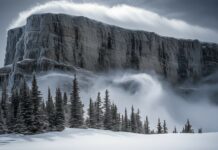 A towering snowy mountain with icy cliffs and swirling snow clouds at the summit.