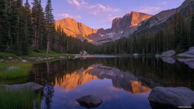 A tranquil Mountain lake mirroring the golden and purple hues of a sunset behind towering peaks.