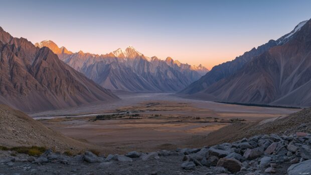 A vast mountain valley surrounded by towering peaks, bathed in soft golden light at sunrise.