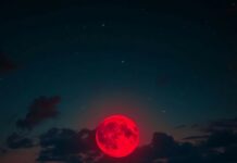 Aesthetic Moon Wallpaper with a mesmerizing red moon hanging low in the night sky over a tranquil beach.