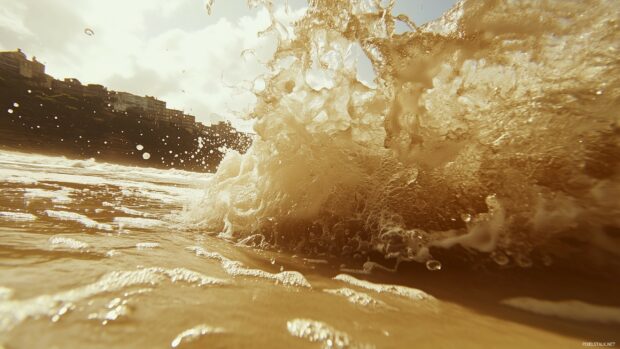 Crashing ocean waves on a sandy beach, with crystal clear water and a bright sky in the background.