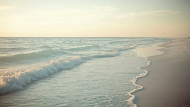 Crashing ocean waves on a sandy beach, with crystal clear water and a bright sky in the background.