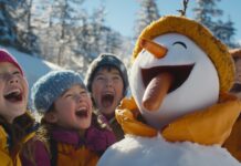 Funny Christmas Wallpaper with a playful scene of a snowman with a carrot nose that has been replaced by a hot dog, with a group of laughing kids enjoying the snowy day.