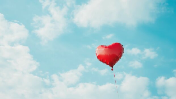 Heart shaped balloon floating in a sky blue background.