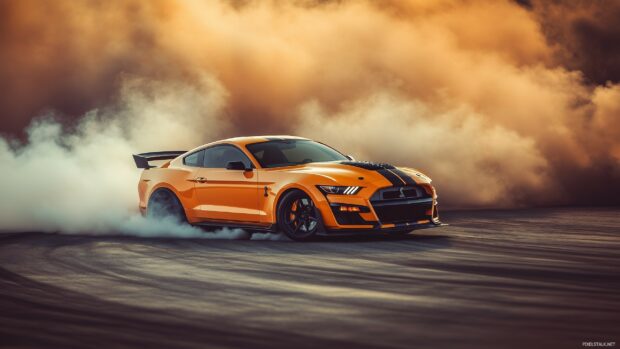 Live Car Wallpaper for desktop with A Ford Mustang Shelby GT500 in fiery orange, drifting through a high speed corner with tire smoke and motion blur effects.