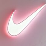 Nike logo with a soft glow effect on a pastel pink background.