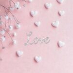 Pink love wallpaper iPhone with the word Love surrounded by small hearts and flowers, set against a soft pastel background.