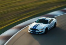 Race car wallpaper HD with a Shelby Mustang GT350 in racing white with blue stripes, speeding through a racetrack with a blurred background emphasizing its speed.