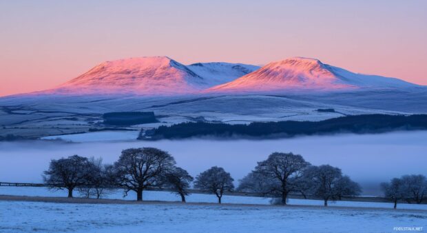 Snowy Mountain peaks illuminated by the soft, glowing amber of a setting sun, with mist drifting through the valleys.