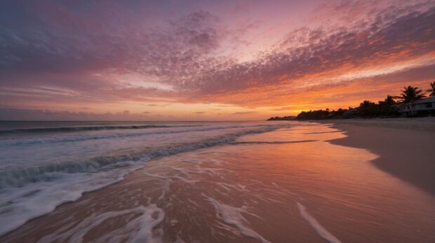 A summer beach sunrise with the first light of day illuminating the sky in shades of pink and orange.