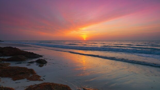 Serene beach sunrise with the first light of day illuminating the sky in shades of pink and orange.